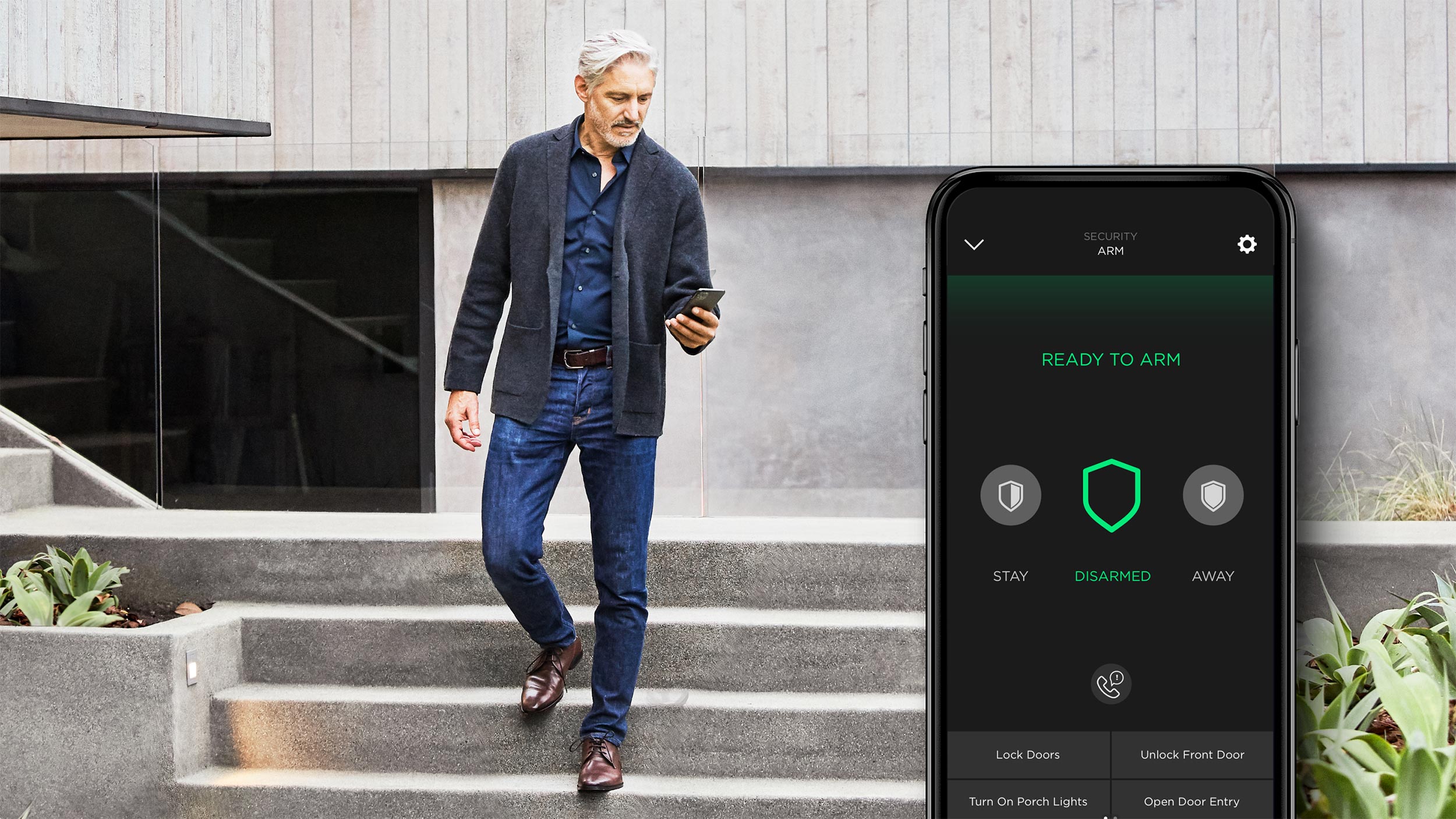 A man walking down steps outside a modern home while checking a security app on his phone.